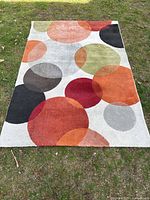 Full view of the rectangular rug showing multi-colored circles on a light background placed outdoors on grass.