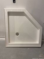 Top view of the white corner shower base showing smooth surface and drainage hole