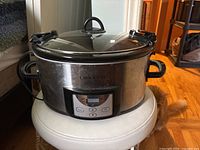 Front view of a Crock-Pot slow cooker, showing digital control panel, side handles, stainless steel body, and glass lid with handle.