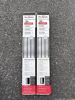 Two unopened boxes of Deckorators Classic 26 inch aluminum deck balusters shown upright on asphalt surface.