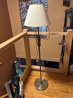 Full view of the floor lamp showing the height, brass base, wooden pole, and beige lampshade.