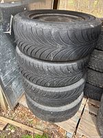 Stack of four Good Year snow tires mounted on rims, showing tread pattern and size, stored in a garage or shed environment.