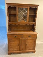 Front view of wooden hutch showing top glass lattice door, open side shelves, drawers, and bottom cabinets.