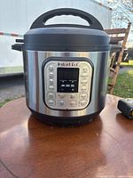 Front view of Instant Pot showing digital control panel with buttons and display screen, stainless steel body with black accents.