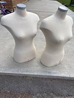 Two female torso mannequins placed on concrete surface outdoors, showing overall condition and size about 27 inches tall. Fabric covered with visible stains and discoloration.