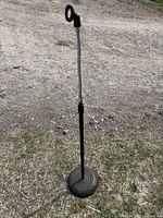Shorter adjustable microphone stand with flexible gooseneck arm and round weighted base shown outdoors on gravel surface.