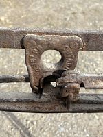 Close-up of metal clamp mechanism with embossed markings on the hay roller frame.