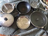 Overview of assorted pots and pans including steamer, frying pans, covered pan, sauce pan and new griddle