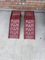 Pair of red metal vehicle ramps placed side by side, view from top and face-up surface showing traction holes.