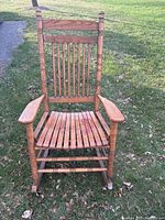 Front view of wooden rocking chair with vertical slat back, turned spindles, and slatted seat showing some wear on seat and rocker.