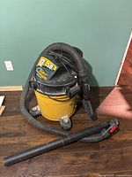 Full view of yellow and black Dirt Hug shop vacuum with attached hose and extension wand placed beside it.