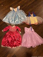 Four princess-style dresses for toddlers size 2-4, various colors and designs, including light blue, red, pink and Snow White inspired.