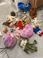 Photo showing assorted stuffed animals including bears, a pony, and various plush toys arranged on a floor.