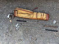 Vintage golf bag with some golf clubs placed outside on rough ground, showing the overall size and condition of the bag and clubs.