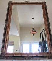 Full view of the large rectangular mirror with gold gilt Florentine frame hanging indoors, showing reflective glass and visible surroundings.