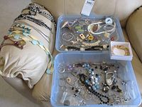 Wide view of assorted costume jewelry including necklaces, bracelets, pins and earrings inside plastic containers and displayed on a pillow