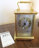 Primary image showing front and top view of vintage gold-tone Bulova carriage clock with Roman numeral face and handle on top.