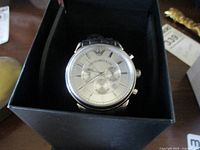 Front view of Emporio Armani men's watch in box showing silver dial with three subdials and Emporio Armani logo at 12 o'clock.