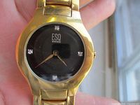 Front view of the gold tone ESQ Swiss men's watch showing black dial with 4 diamond markers at 12, 3, 6, and 9 positions and gold hands.