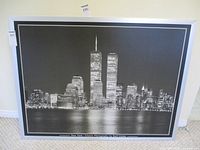 Frontal view of the black and white photograph showing the New York skyline including the Twin Towers, in a frame on a floor against a wall.