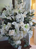 Front view of large ceramic urn planter with huge bouquet of white artificial flowers including calla lilies, roses, and greenery.