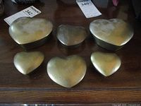 Set of six heart-shaped brass boxes arranged in two rows showing tops with lids on, displaying variation in size and patina.