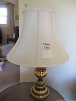 Full view of mid-century modern brass table lamp with cream-colored fabric shade on a table.