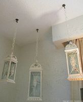 Three white distressed metal and glass hanging candle holders suspended from ceiling hooks with chains in a textured wall room.
