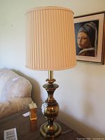 Lamp unlit showing brass base and pleated cream shade in natural light.