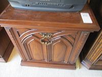 Front view of vintage wooden side table cupboard showing carved panel doors and brass decorative handle.