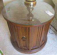 Top view of the round wooden table cupboard with its smooth circular glass top and brass ring pull hardware.
