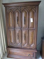Front view of the vintage wooden highboy chest with double doors and single drawer base, showing wood paneling and brass handles.