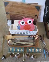 Full view of the mixed lot showing cutting boards, crocheted owl pot holder, plastic basket, kitchen utensils, glass napkin holder, and ceramic decorative napkin holders.