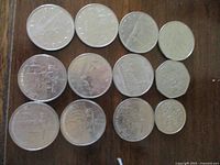 Top view of eleven Canadian coins including seven one dollar coins showing Voyageur canoe design, and smaller coins with floral emblems, laid on wooden surface.