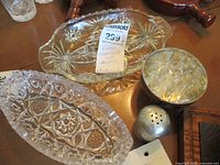 Overview of vintage crystal and glass items including two oblong crystal dishes, glass flower frog in metal holder, and small metal shaker.