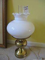 Full view of vintage brass and milk glass lamp with clear glass chimney on top, showing the ruffled milk glass shade and reflective brass base.