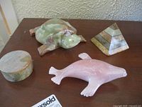 Lot of four vintage marble and alabaster decorative items including two animal figurines, a round box, and a pyramid on a brown surface.