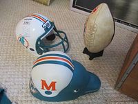 Photo showing vintage Miami Dolphins football helmet with teal facemask and team logo, alongside large dolphin head display painted with helmet and 'M' logo.