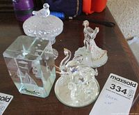 Overall view of the lot showing dancing couple, duck-shaped covered dish, rectangular etched crystal block, swan, and elephant figurines.
