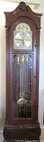 Full view of the vintage grandfather clock showing wooden cabinet, glass front, pendulum, weights, and clock face.