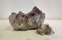 Front view showing large amethyst crystal cluster and smaller clear crystal piece placed side by side on carpeted surface.