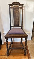 Front view of antique Jacobean style wooden chair showing high back with carved decorative top and twist carved legs with purple velvet seat cushion.