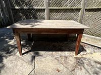 View of the full antique pine harvest table showing the rectangular top, broad plank construction, and sturdy square legs in an outdoor patio setting.