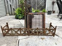 Three rusted steel garden art pieces consisting of a low fence piece, square floor grate, and tall ornate standing piece.