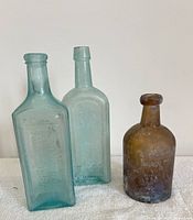 Three antique tumbled glass bottles grouped; two blue rectangular with embossed text, one smaller amber round bottle