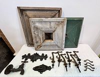 Three square handmade wooden wall tiles and various antique hardware pieces displayed on a white cloth.