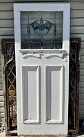 Full front view of the white antique solid wood door with stained glass insert window and hand carved details below the window.