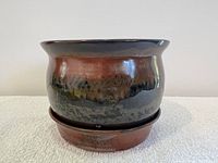Side view of the artist-made pottery berry bowl in glazed earthy tones with round shape and flared rim, sitting on its matching dish.