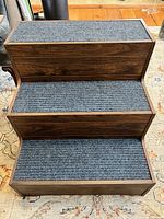Top view showing three carpeted steps on dark wooden stairs.