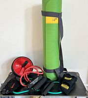 Photo showing the green Lole yoga mat rolled up and secured with carrying strap, alongside Everlast weighted gloves, Nike weighted gloves, two exercise bands, and red ab roller.